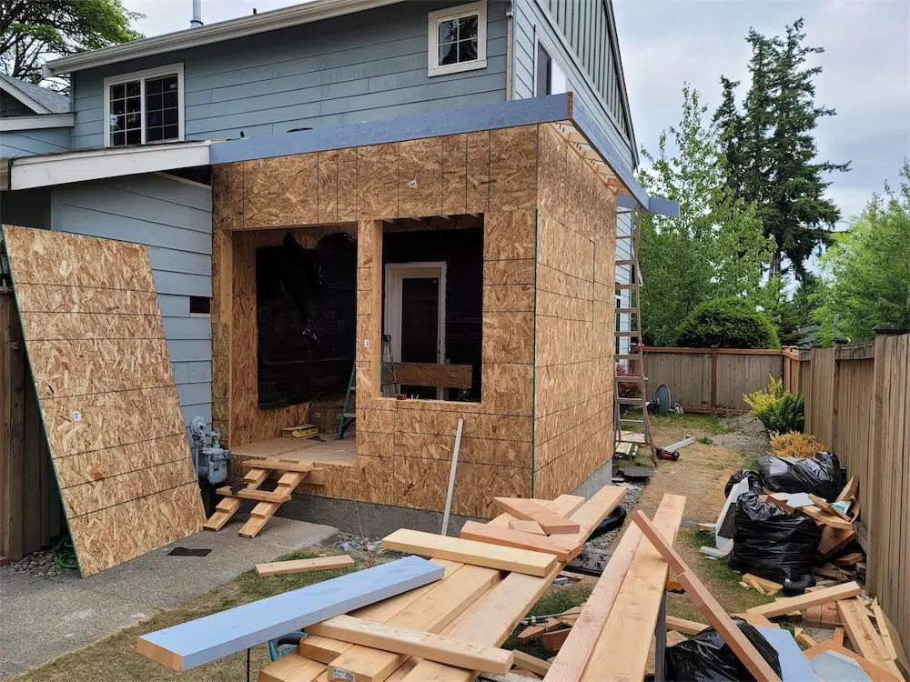 House addition under construction with sheathed framing and large window openings