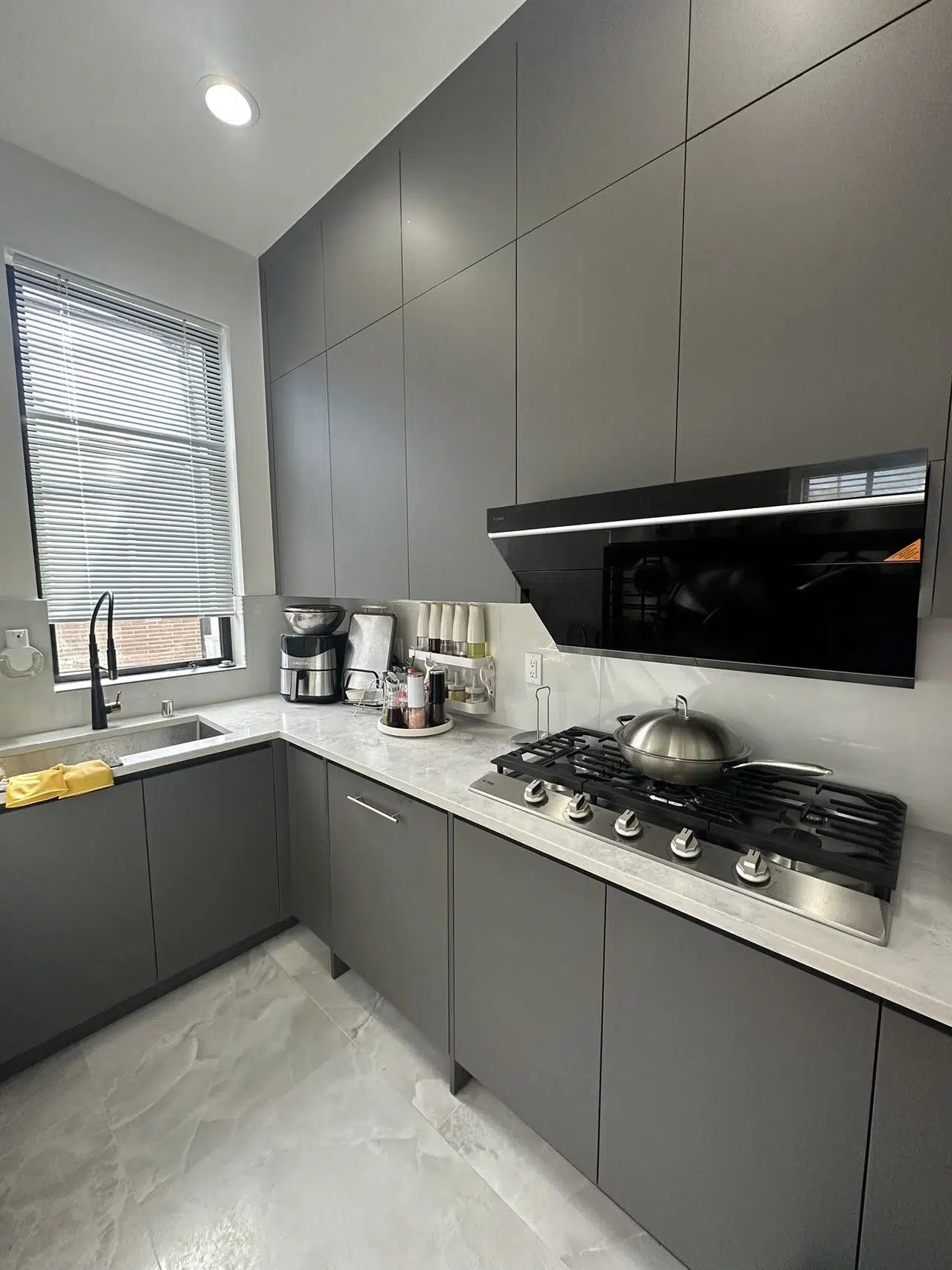 Gray kitchen cabinets with a gas cooktop, wall-mounted hood and light backsplash